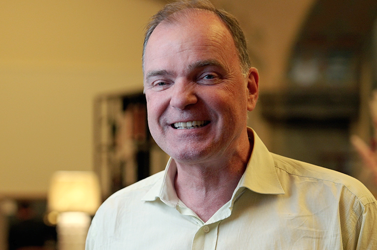 En smilende mand med kort brunt hår iført en lys skjorte med knapper.