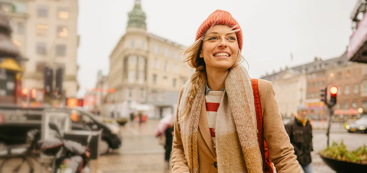 Foto af en smilende ung kvinde, der cykler rundt i byen en kold vintermorgen.
